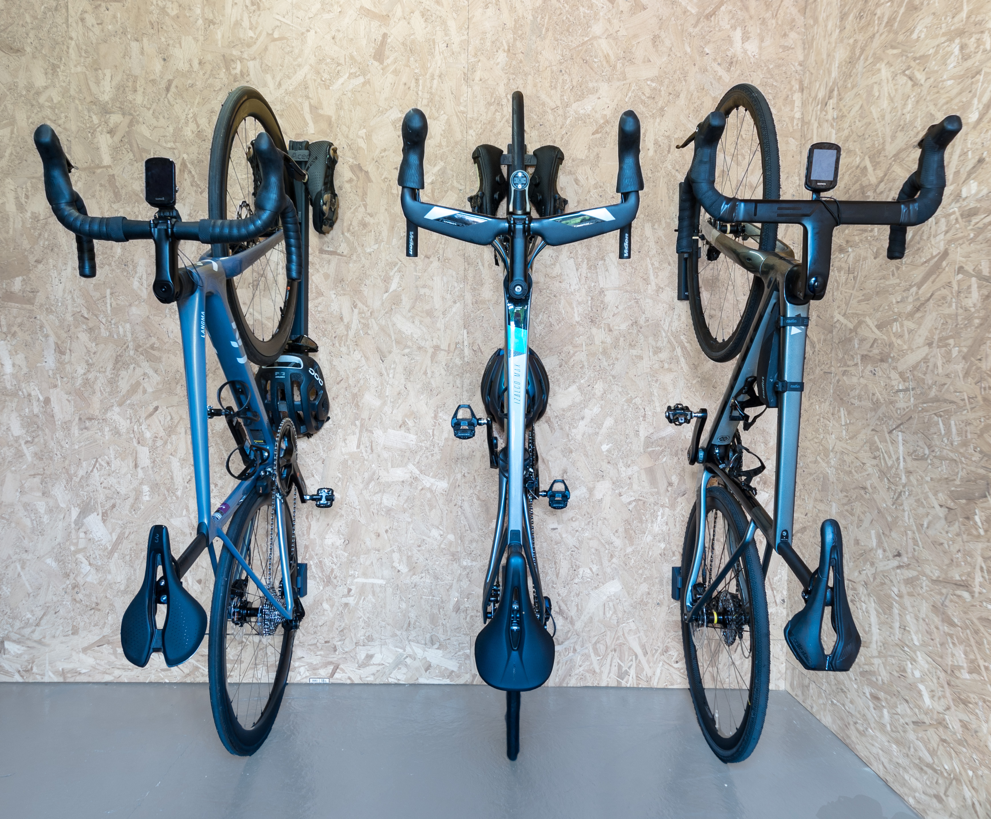 Storage saving upright bike railds from PLAced Three bikes lined up and stored vertically using the PLAced rail system. Two bikes use the extended rails which are holding the riders helmets, sunglasses and cleats.