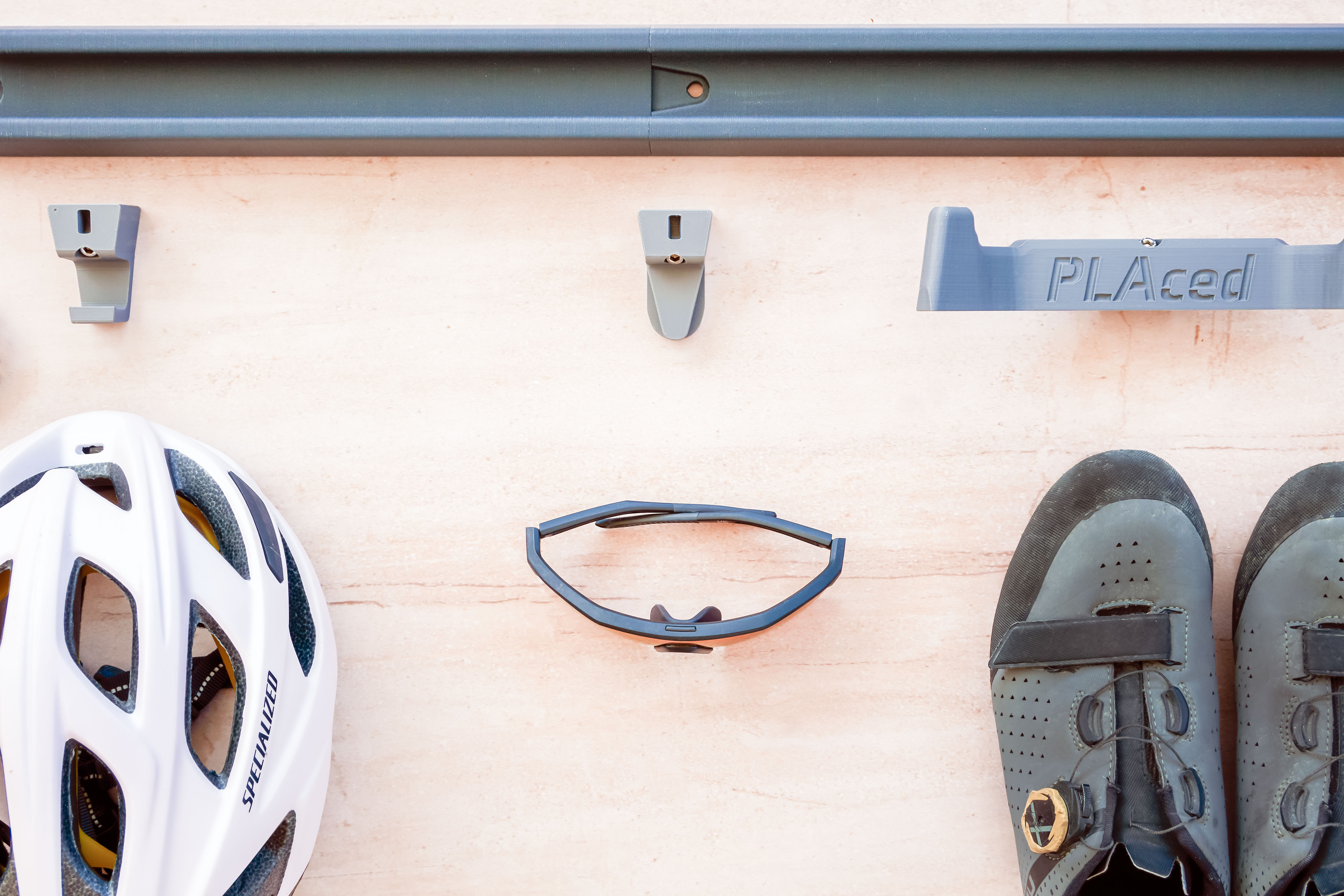 The Verticale Upright Rail Ready for installation Cycling Kit: White Helmet, Glasses and shoes layout out underneath The Verticale upright rail system ready to be installed on the wall. Below the rail are the hooks ready for installation